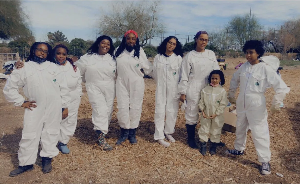 Eight women and a child in white beekeeping suits standing together outdoors at a BaeHive training